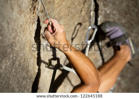 A man with strong muscles and sweating palms climbs a steep rock face, secured by a rope above. The adrenaline of the sport is palpable.