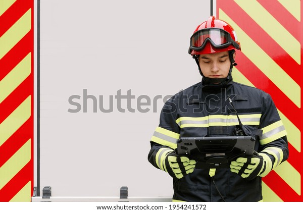 A man of strong physique in uniform and helmet\
stands by a rescue vehicle.