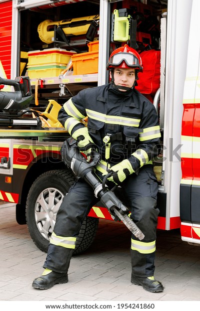 A man of strong physique in uniform\
and helmet stands by a rescue vehicle. Man\
rescuer