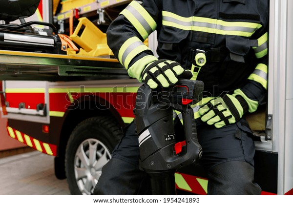 A man of strong physique in uniform\
and helmet stands by a rescue vehicle. Man\
rescuer