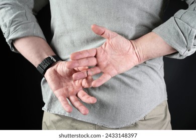 Man in struggling to remove wedding ring from his finger, close-up holding hands behind his back. Husband betrayal concept