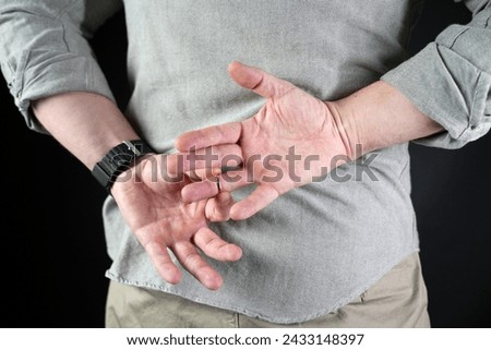 Man in struggling to remove wedding ring from his finger, close-up holding hands behind his back. Husband betrayal concept