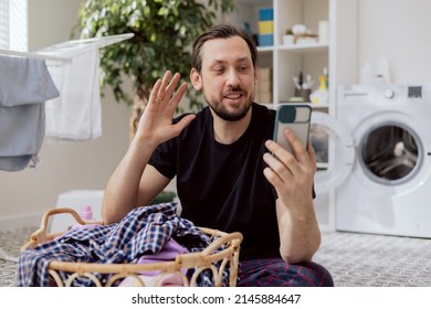 Man With Stubble Sits On Bathroom Floor, Laundry Room Performs Household Chores, Sorting Colorful Clothes For Washing, Man Talks On Phone On Video With Mom, Swipes At Smartphone Camera.