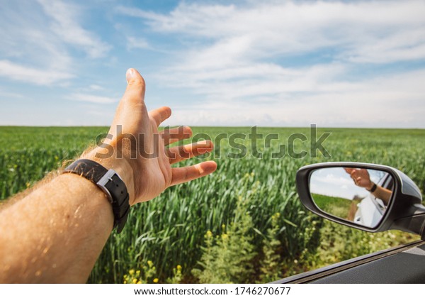 a man stuck his hand out of a\
car window while driving in sunny weather among green\
fields