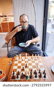 Man studying chessboard while sipping tea, intense focus on midgame position, upright posture and analytical gaze, coffee shop interior with muted tones, strategy practice and quiet concentration
