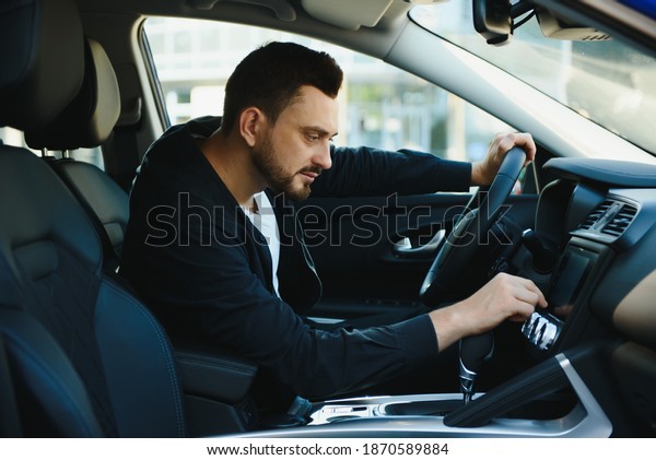Man of style and status. Handsome young man\
in full suit smiling while driving a\
car