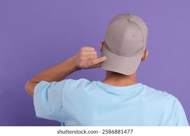 Hombre en elegante gorra de béisbol sobre fondo violeta, vista posterior. Maqueta para el diseño