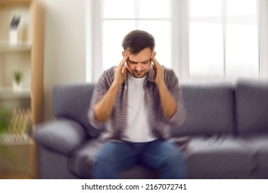 Man suddenly feels dizzy and takes a seat on the sofa. Young guy feeling pain and spinning sensation in his head. Headache, vertigo, health problem, brain tumor concept - Shutterstock ID 2167072741