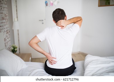 Man Suffering From Back Pain At Home In The Bedroom.