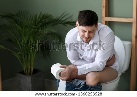 Man suffering from diarrhea while sitting on toilet bowl at home