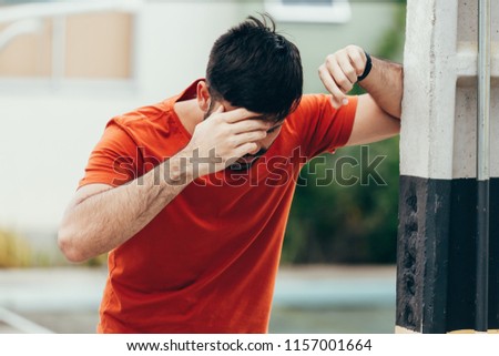 Man suffering from dizziness with difficulty standing up while leaning on wall