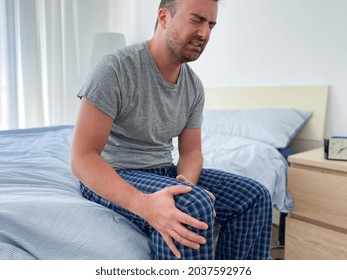 Man Suffering From Knee Pain Sitting On The Bed