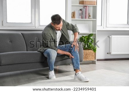 Man suffering from pain in leg on sofa at home