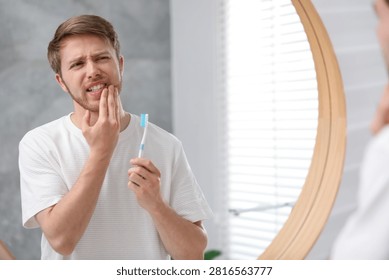 Man suffering from pain while brushing teeth in bathroom