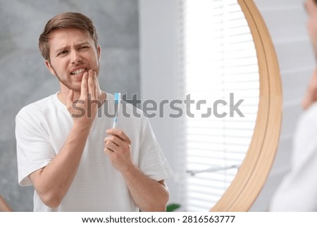 Man suffering from pain while brushing teeth in bathroom
