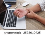 Man suffering from pain in wrist while working on laptop at table indoors, closeup. Carpal tunnel syndrome