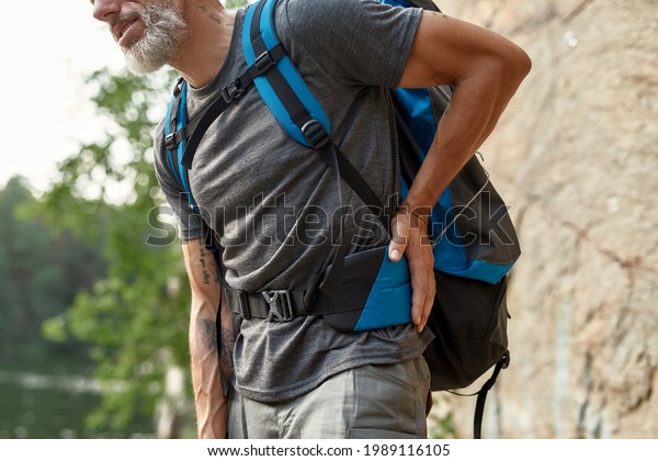 Man suffering from small of back\
aching during trekking in summer nature, close up, cropped. Hiking,\
travel outdoor, recreation and active adventure\
concept