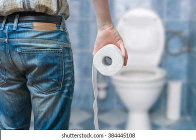 Man suffers from diarrhea holds toilet paper roll in front of toilet bowl.