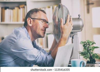 Der Mensch leidet an Hitze während der Arbeit im Büro und versucht, sich vom Lüfter abzukühlen
