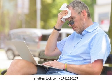 Man Suffers From Heat While Working With Laptop Outside And Wiping His Forehead With Tissue