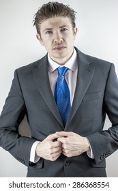 A Man In A Suit With A Blue Tie, And Slicked Back Hair Poses In A Studio.