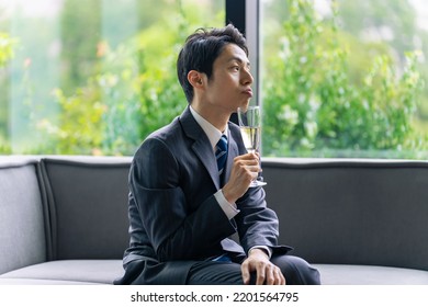 A Man In A Suit Drinking Champagne With An Unimpressed Expression.