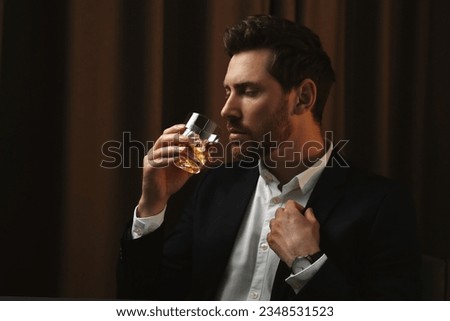 Man in suit drinking whiskey with ice cubes from glass on brown background