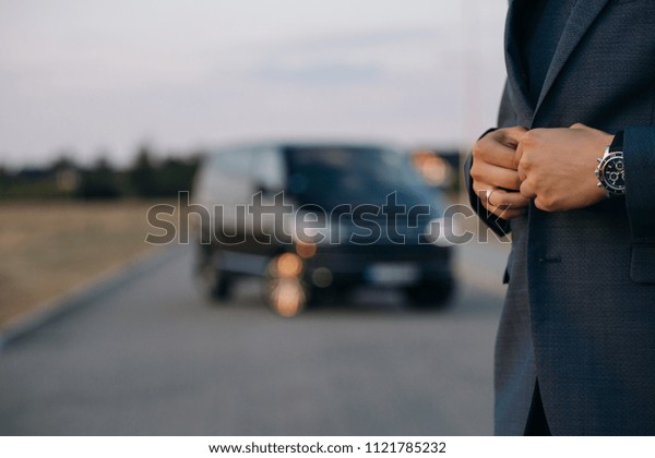 Man in suit in front of\
luxury car minivan at the background. Driver of the car is waiting\
for passenger 