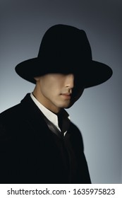 Man In Suit And Hat In Shadow Against Dark Background. Silhouette Of A Mysterious Man In Fedora Hat. Incognito Portrait