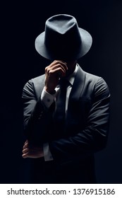 Man in suit hiding face behind his hat isolated on dark background. secret and incognito concept                  - Shutterstock ID 1376915186