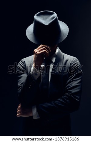 Man in suit hiding face behind his hat isolated on dark background. secret and incognito concept                 