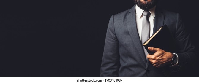 Man In Suit Holding A Bible In His Arm On A Black Background