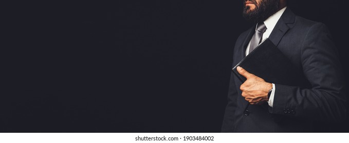 Man In Suit Holding A Bible In His Arm On A Black Background