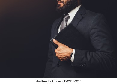 Man In Suit Holding A Bible In His Arm On A Black Background