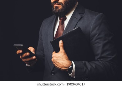 Man In Suit Holding A Bible In His Arm And With The Cell Phone In Hand