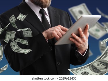A man in a suit is holding a digital tablet and dollars are falling from the sky. - Shutterstock ID 2029612430