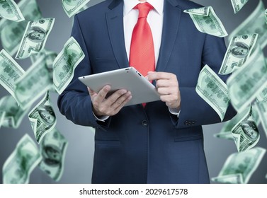 A man in a suit is holding a digital tablet and dollars are falling from the sky. - Shutterstock ID 2029617578