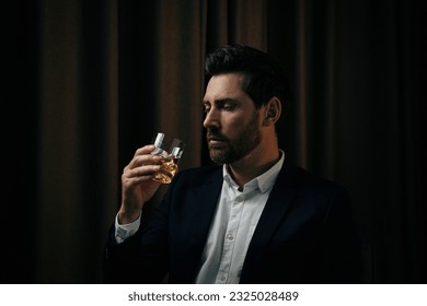 Man in suit holding glass of whiskey with ice cubes on brown background