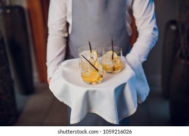 Man in suit holding silver tray with glasses of whiskey