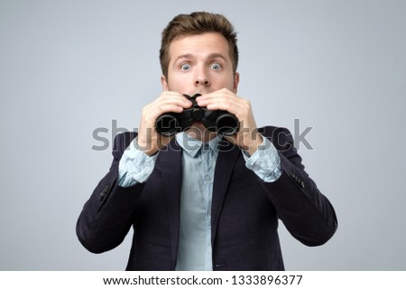 Man in suit looking through binoculars with shock and wonder. Studio shoot.