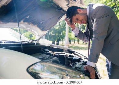 Man In Suit Looking Under The Hood Of Breakdown Car Outdoors