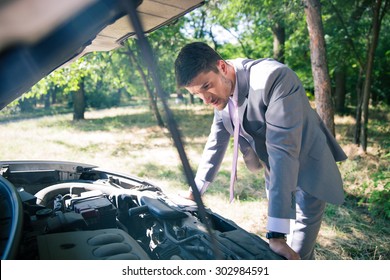 Man In Suit Looking Under The Hood Of Breakdown Car