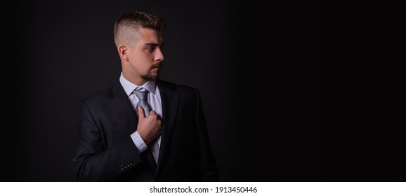 Man In A Suit On A Black Background Adjusts His Tie