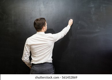 Man In Suit Pointing Something On Chalkboard,back View,isolated.Copyspace Blank.Teacher Writing On Black Board