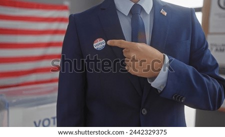 A man in a suit points to a 'voted' sticker with an american flag backdrop in a voting center.