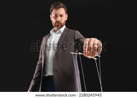 Man in suit pulling strings of puppet on black background, low angle view