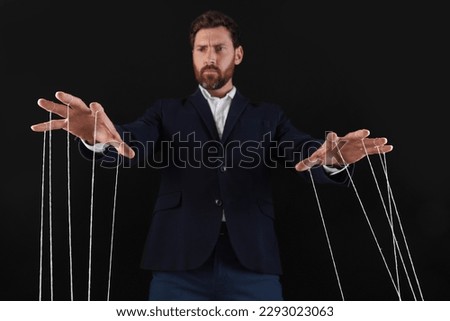Man in suit pulling strings of puppet on black background, low angle view