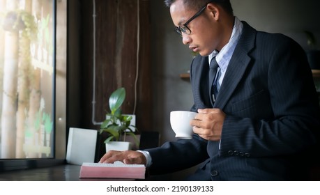 Man In A Suit Reading Bible And Holding Coffee Cup.