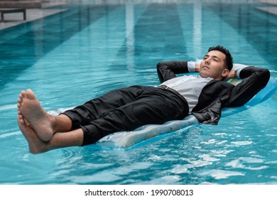 A Man In A Suit Is Resting In The Pool On An Inflatable Blue Mattress