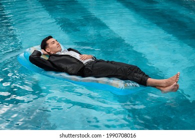 A Man In A Suit Is Resting In The Pool On An Inflatable Blue Mattress